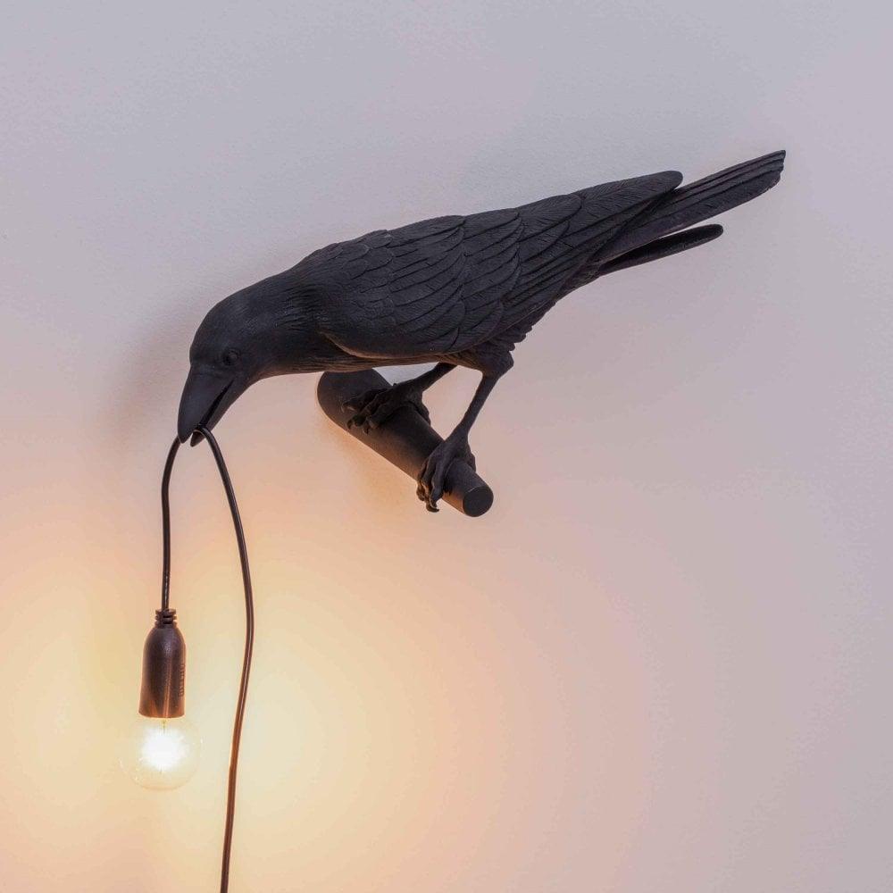 Set against a warm cream gradient, this black Clérachic bird lamp spreads its wings with the bulb glowing below.