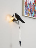 Closer in on the same room corner, this black Clérachic bird lamp lights its bulb warm beneath a framed abstract print.