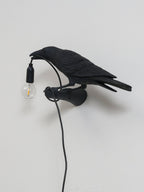 Side-on against a plain grey wall, this black resin bird from Clérachic holds an unlit clear bulb by its cord.