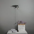 Above a bedside table with dried flowers and stacked books, this black Clérachic bird lamp casts a small warm glow.