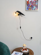 Beneath a colourful framed print, this black Clérachic bird lamp lights a round side table below with warm light.
