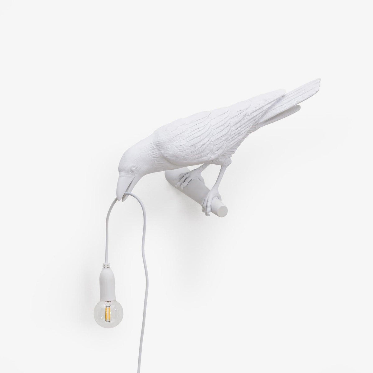 This white resin Clérachic bird lamp perches with its mount visible, beak lowered to a warmly lit hanging bulb.