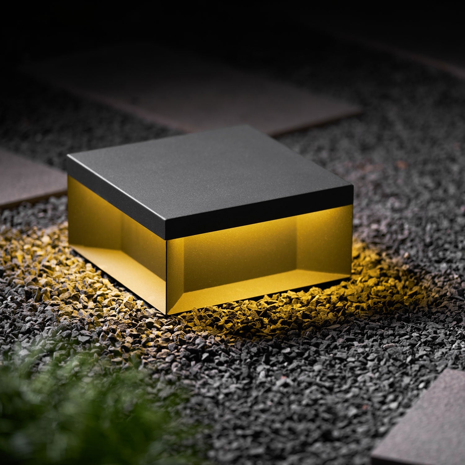 Boxy black outdoor lamp with warm light in a garden