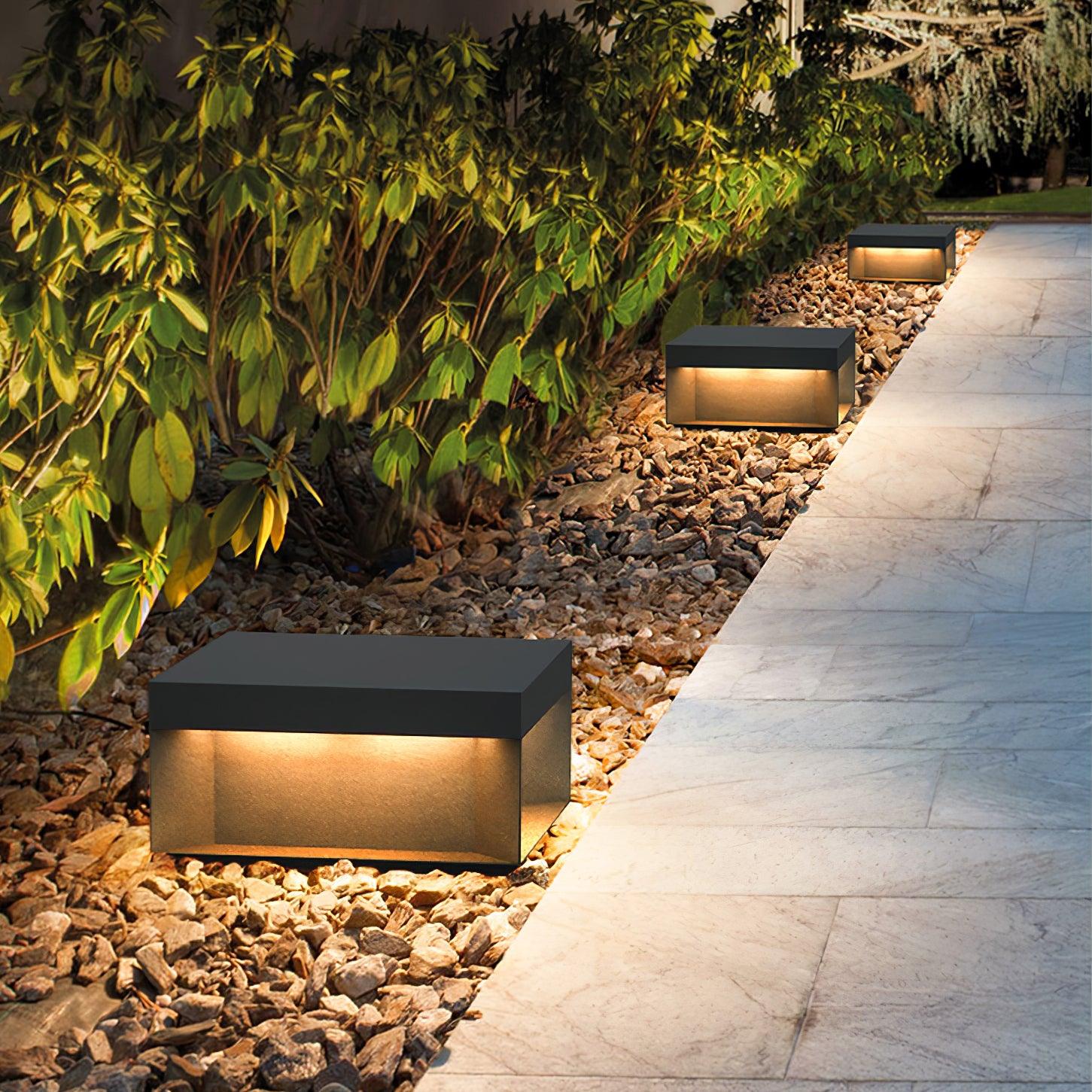 Black box outdoor light with warm even glow on a lawn
