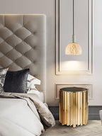 Clérachic alabaster pendant light beside a cream tufted headboard and a fluted gold side table, its dome lit a soft white.