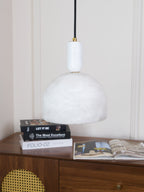 The unlit alabaster dome of this Clérachic pendant hangs above the same book-topped sideboard, its smoother white stone shown in daylight.