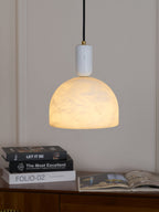 Photographed above a wooden sideboard stacked with books, the lit alabaster dome of this Clérachic pendant casts a warm glow.