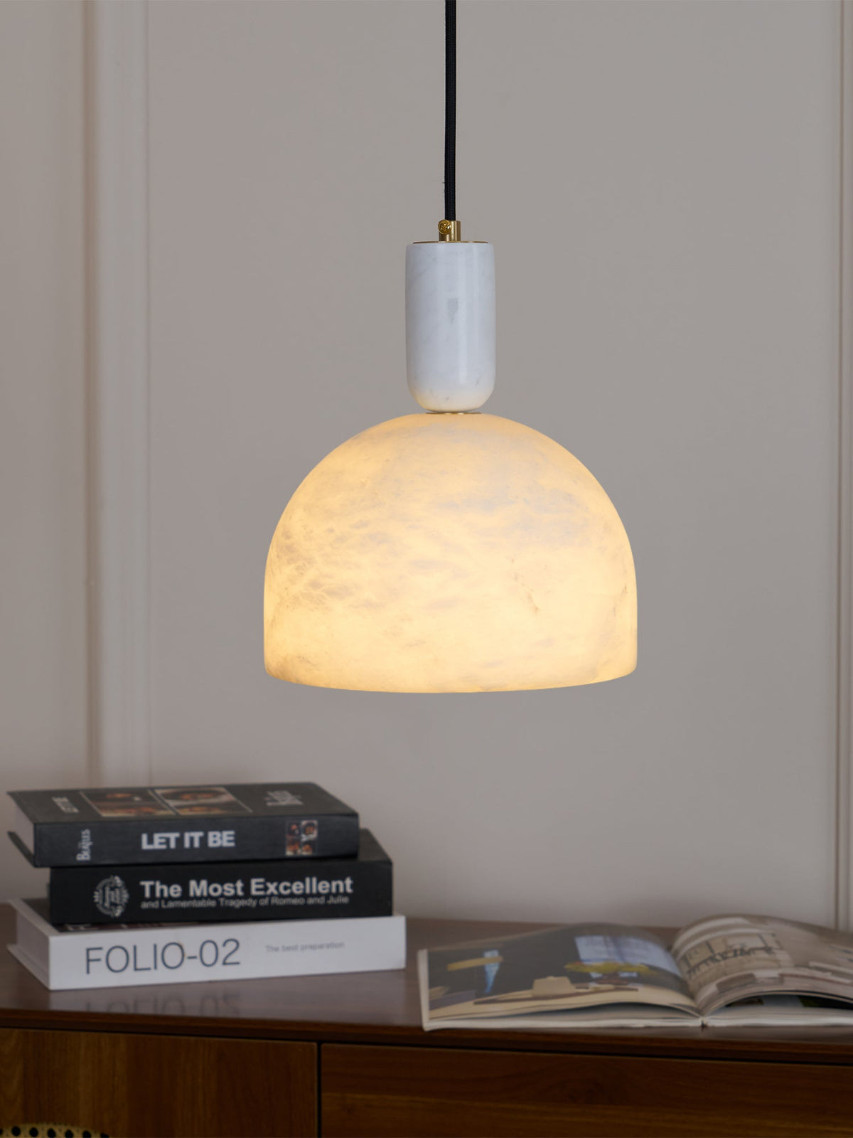 Photographed above a wooden sideboard stacked with books, the lit alabaster dome of this Clérachic pendant casts a warm glow.