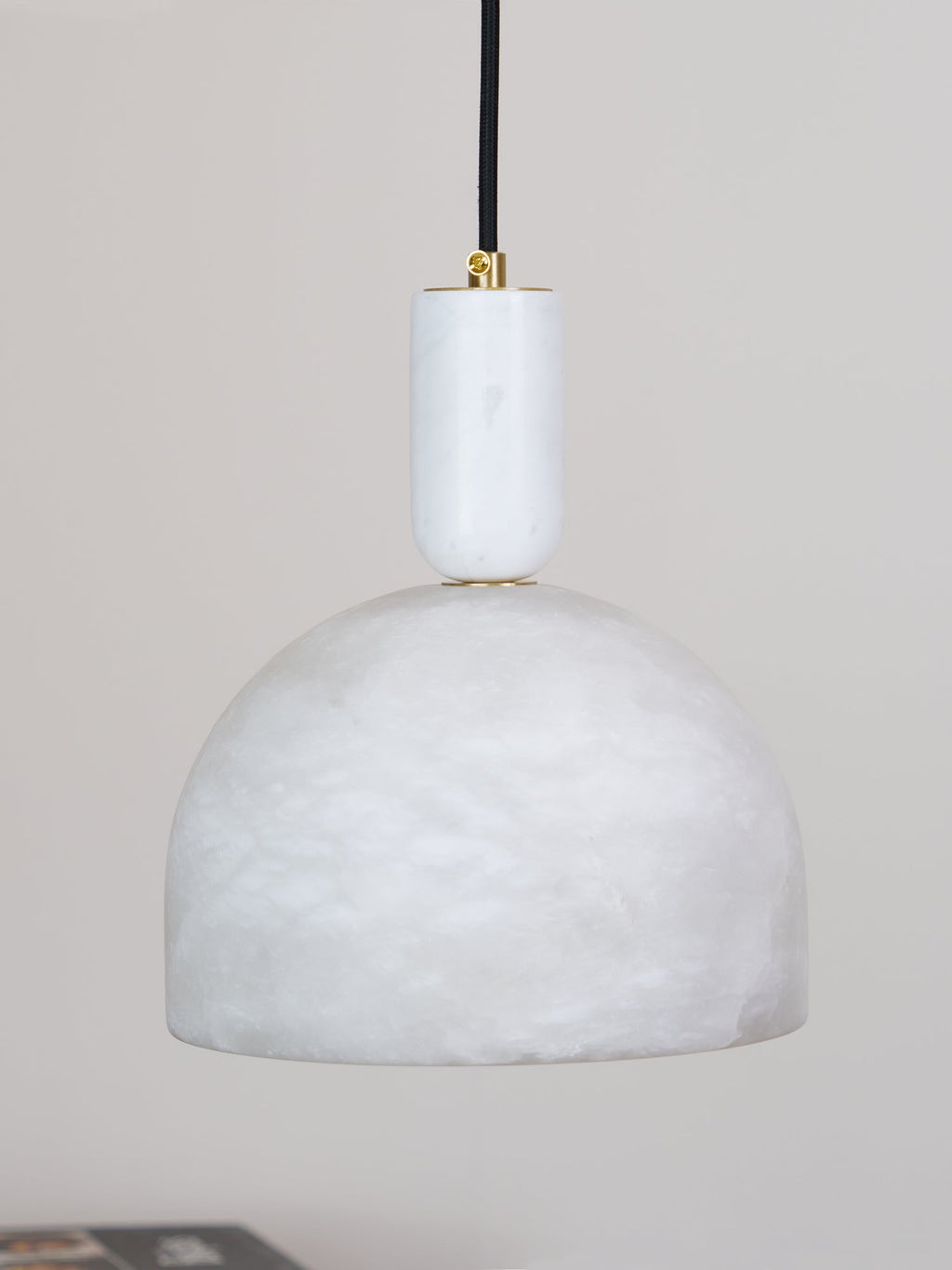 A close, unlit view shows the smooth white alabaster dome and short brass neck of this Clérachic pendant against a grey backdrop.