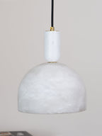A close, unlit view shows the smooth white alabaster dome and short brass neck of this Clérachic pendant against a grey backdrop.