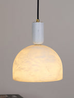 Lit against a plain grey backdrop, this Clérachic alabaster dome pendant shows faint veining as light passes through the stone.