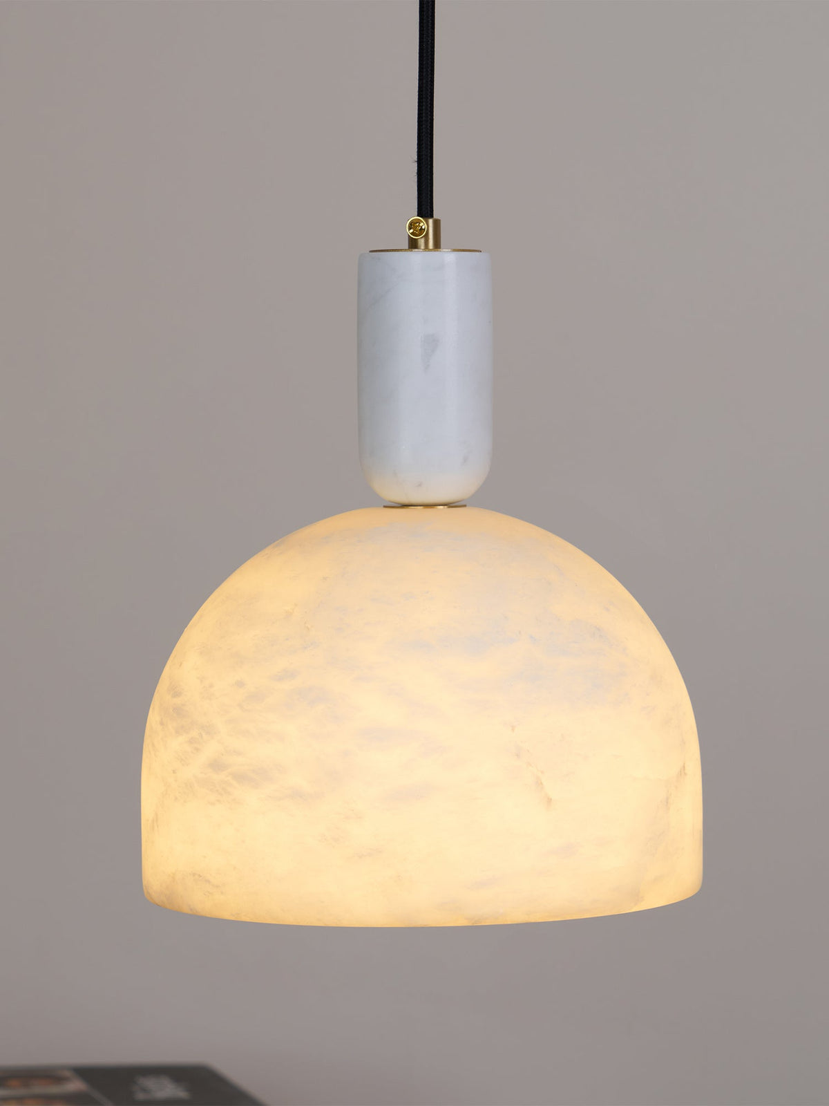 Lit against a plain grey backdrop, this Clérachic alabaster dome pendant shows faint veining as light passes through the stone.