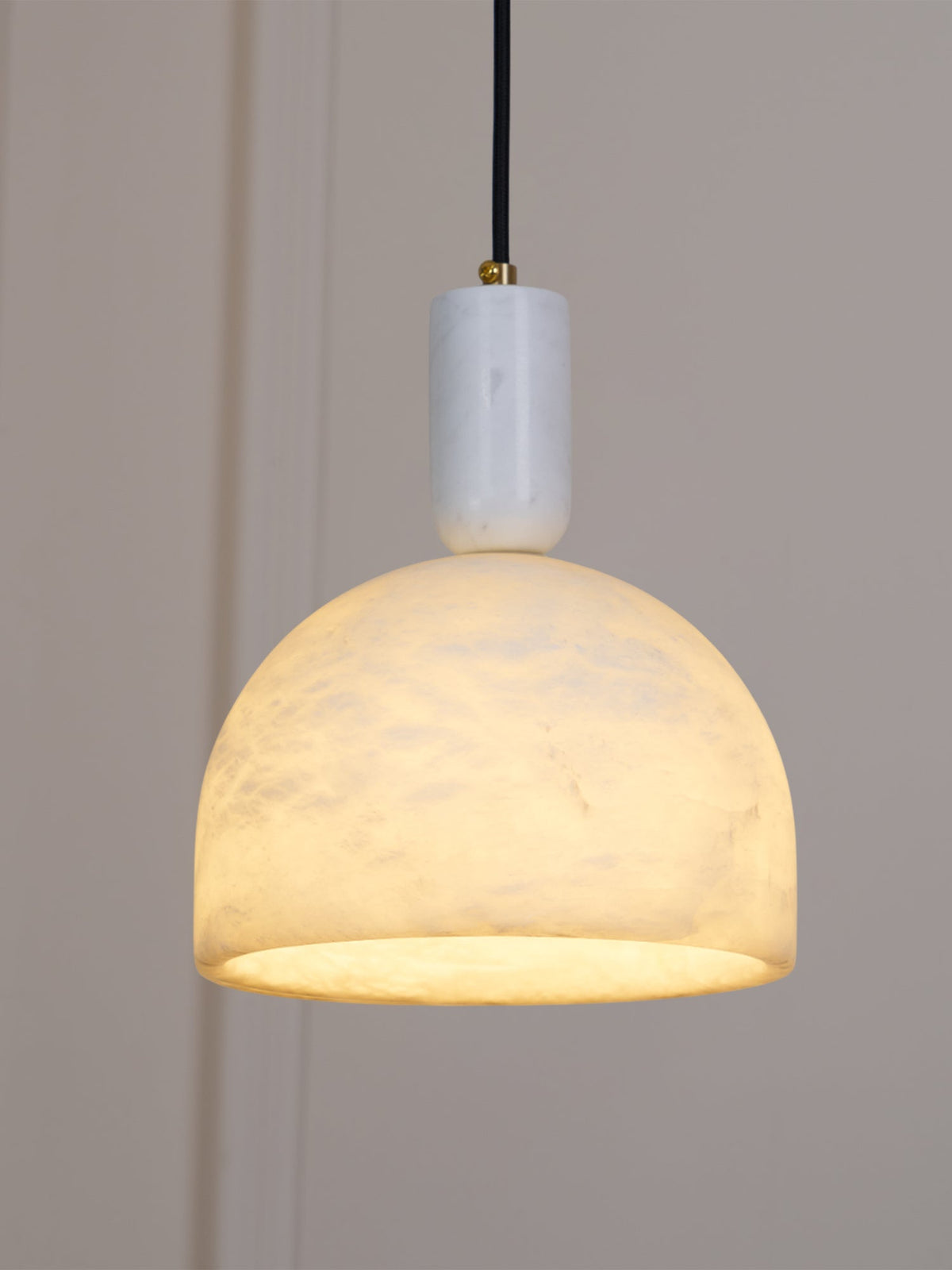 Hung near a panelled wall and switched on, this Clérachic alabaster dome glows amber above its brass neck and black cord.