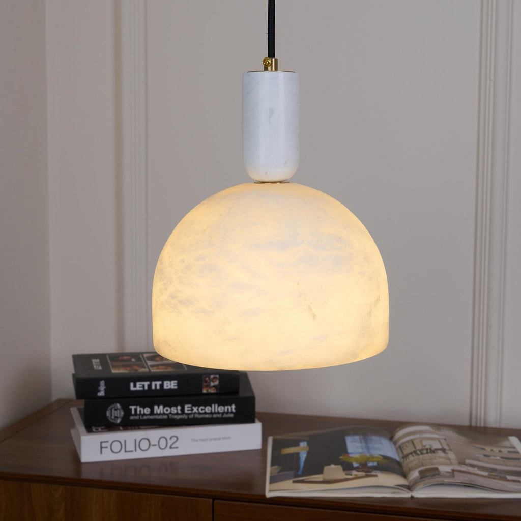 Clérachic alabaster pendant light hanging low over a wooden sideboard stacked with books, its dome close enough to show full texture.
