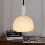 Clérachic alabaster pendant light hanging low over a wooden sideboard stacked with books, its dome close enough to show full texture.