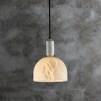 Clérachic alabaster pendant light hanging against a dark, mottled plaster wall, the cord and brass fitting clearly visible.