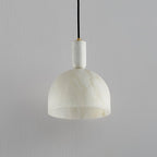 Clérachic alabaster pendant light unlit against a plain wall, showing the shade's pale, matte stone finish in daylight.