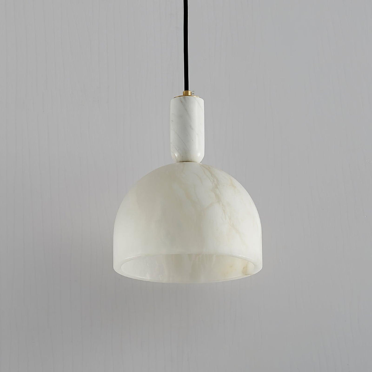 Clérachic alabaster pendant light unlit against a plain wall, showing the shade's pale, matte stone finish in daylight.