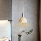 Clérachic alabaster pendant light against a textured plaster wall, hanging near a floor vase of foliage and red berries.