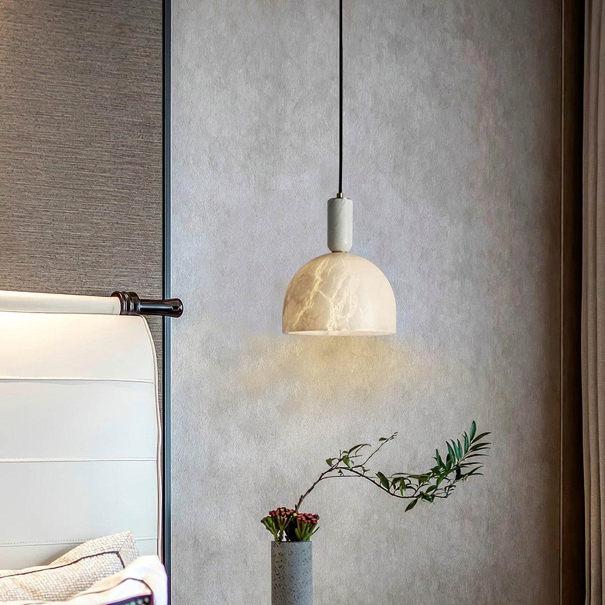 Clérachic alabaster pendant light against a textured plaster wall, hanging near a floor vase of foliage and red berries.
