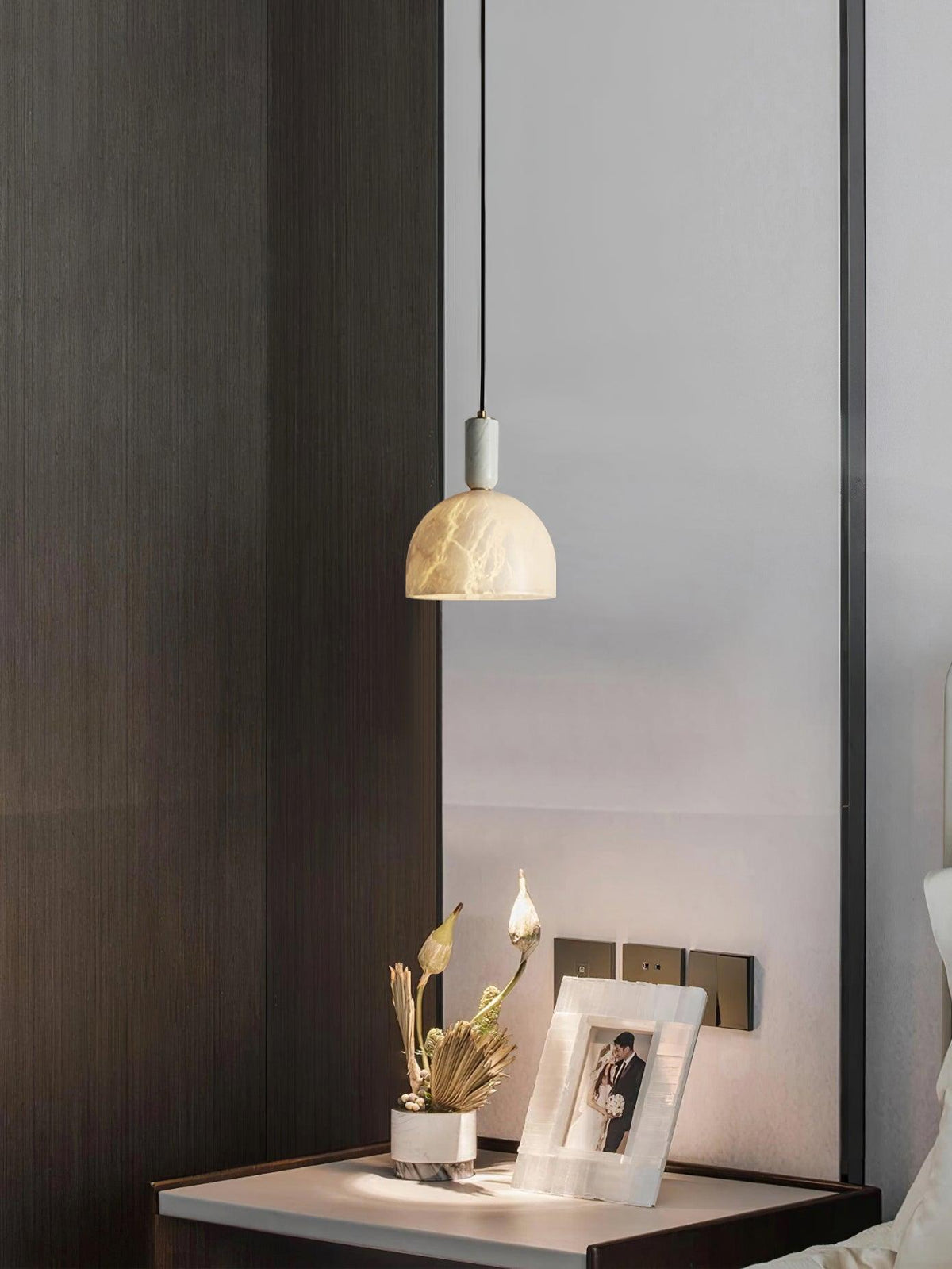 Clérachic alabaster pendant light glowing above a bedside table set with dried flowers and a small framed photograph.