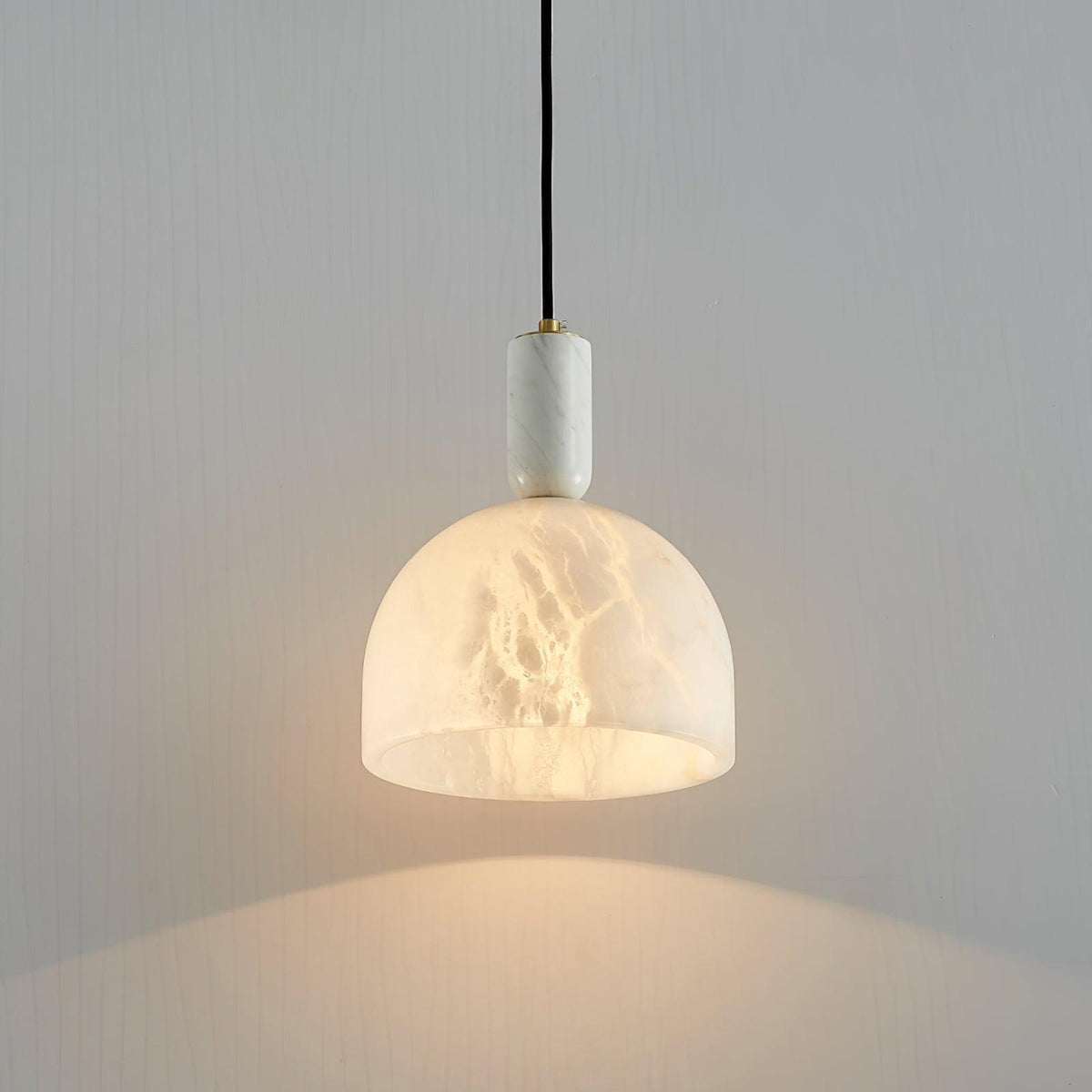 Clérachic alabaster pendant light against a plain grey wall, its dome shade glowing softly with no other furniture in view.