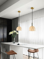 Two Clérachic alabaster pendant lights hang over a white kitchen island with leather barstools and a vase of white lilies.