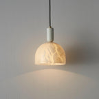 Close wall view of the Clérachic alabaster pendant light lit brightly, the natural veining in the stone shade clearly visible.