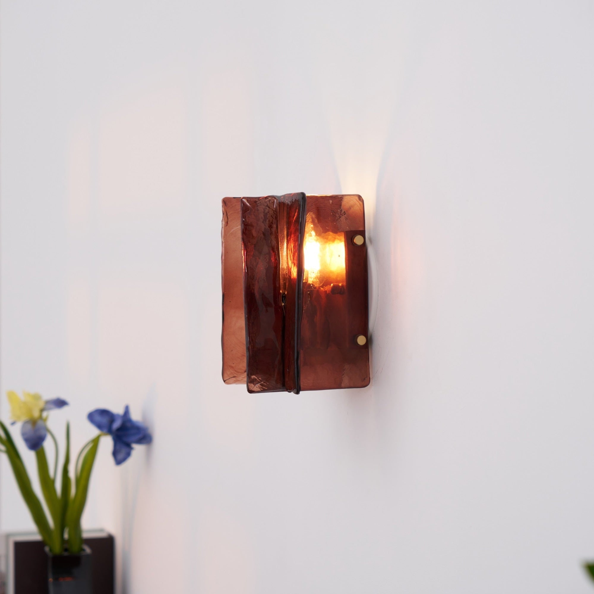 Brass and wine red glass wall sconce lit in a dim room