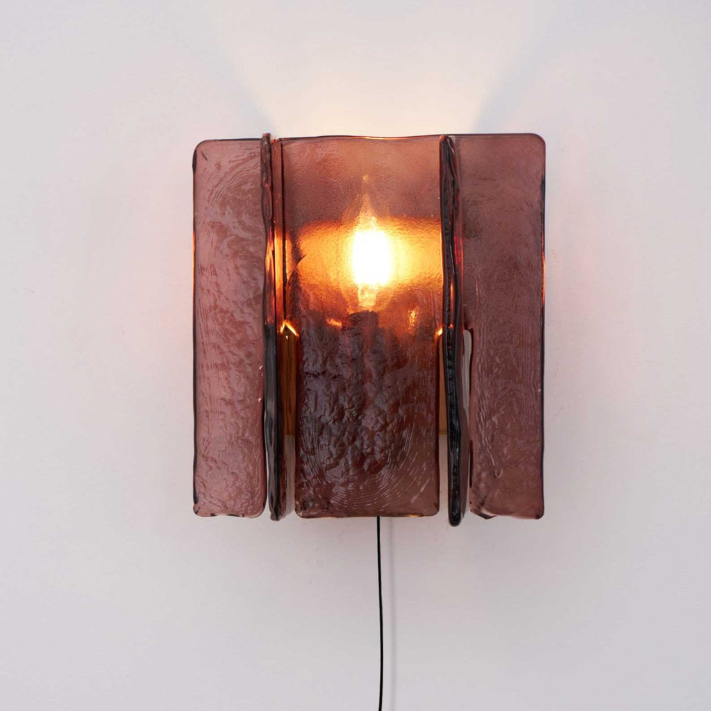 Wine-red glass wall sconce with warm brass body glowing softly