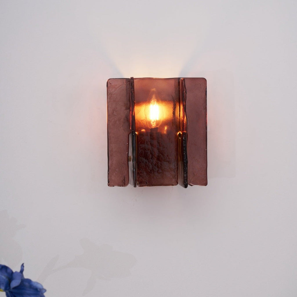 Lit brass wall sconce projecting dramatic patterns onto the wall