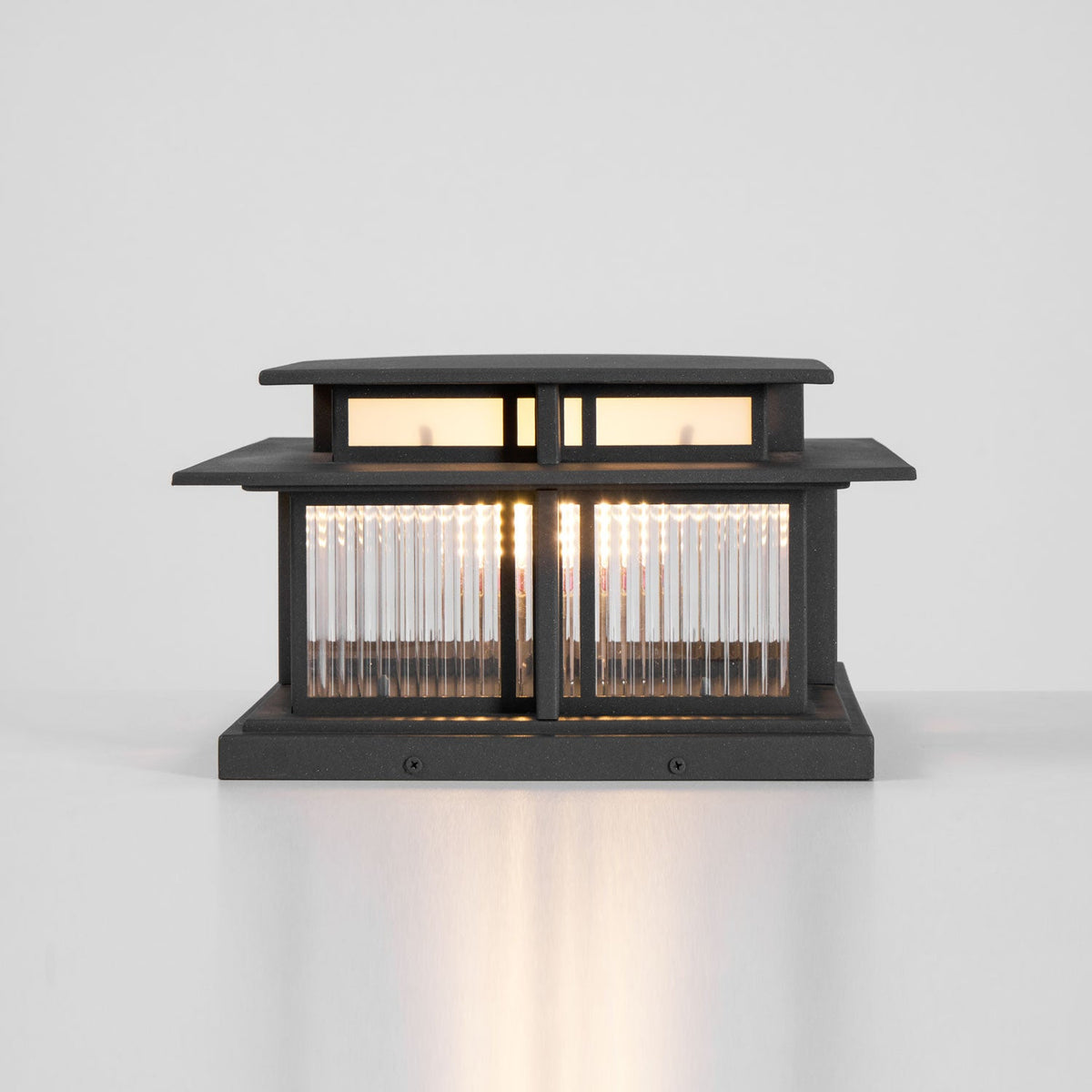 This lit Clérachic pillar light shows its fluted glass panels and mounting screws in the base, set against plain white.