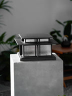At night, this lit Clérachic pillar light sits on a raised stone plinth in a garden, fluted glass panels aglow.