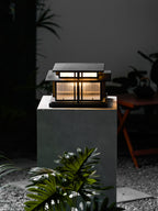 Low-angle view of this lit Clérachic pillar light on a stone plinth, tropical foliage framing it at night.