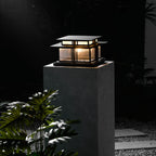 A taller framing shows this lit Clérachic pillar light glowing atop its stone plinth among dark garden foliage.