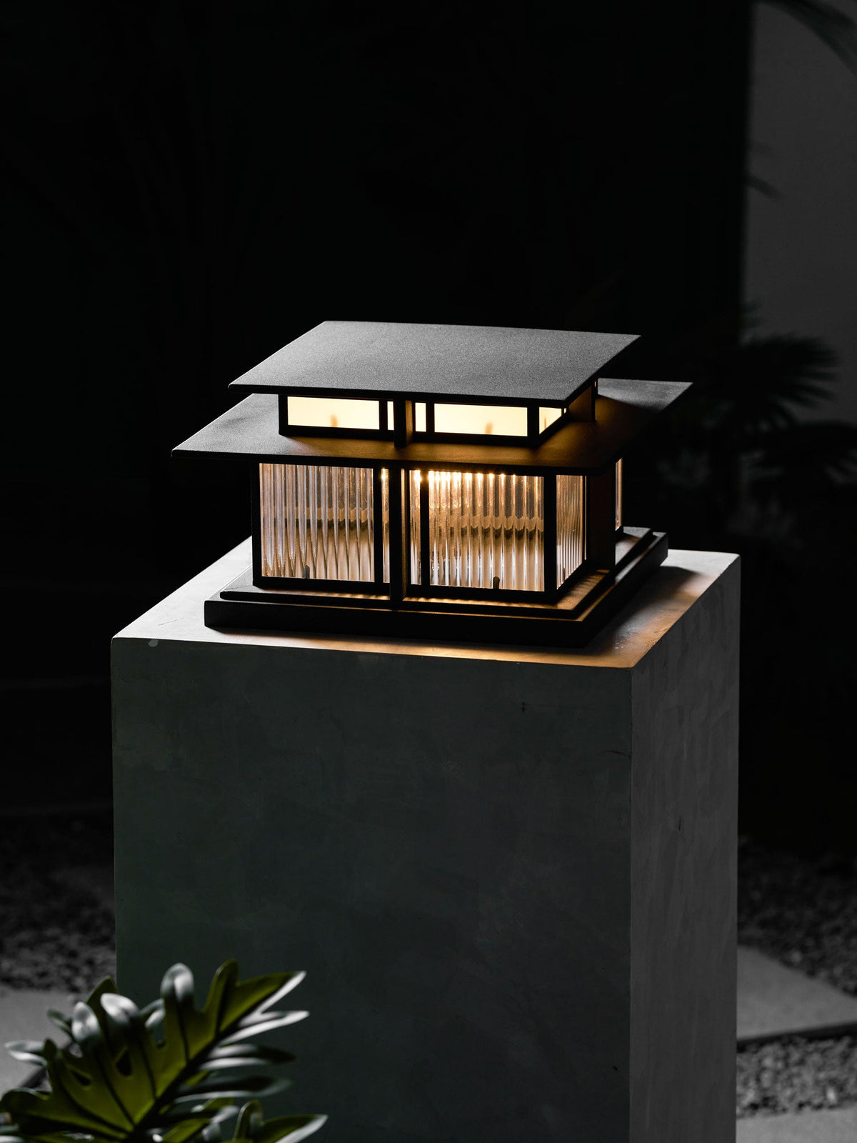 Another night view of this lit Clérachic pillar light on a stone plinth, its fluted glass panels casting a warm glow.