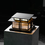 Viewed from above, this lit Clérachic pillar light sits on a pale stone plinth, its glow set against a dark garden.