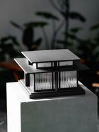 A close angled view of this lit Clérachic pillar light on its stone plinth, dark foliage surrounding it.