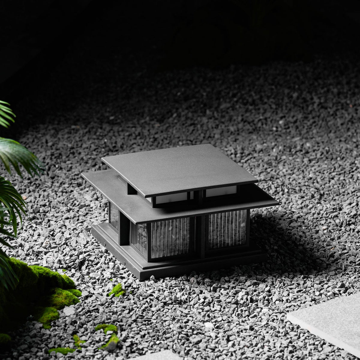 Set among gravel and moss, this lit Clérachic pillar light glows quietly in a shaded garden corner.