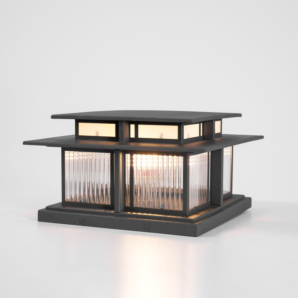 A three-quarter studio view of this lit Clérachic pillar light, fluted glass panels glowing above a screwed-down base.