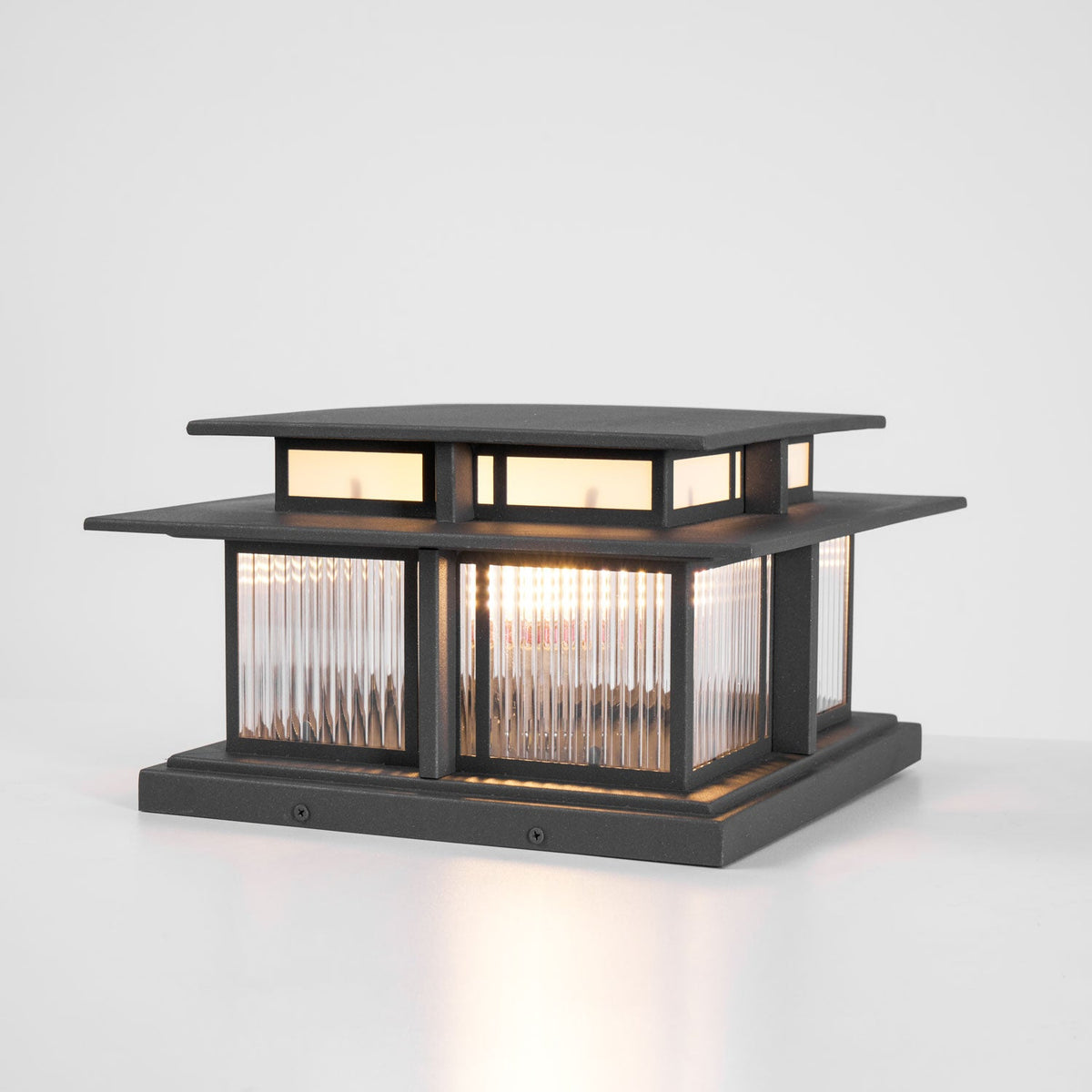 A three-quarter studio view of this lit Clérachic pillar light, fluted glass panels glowing above a screwed-down base.