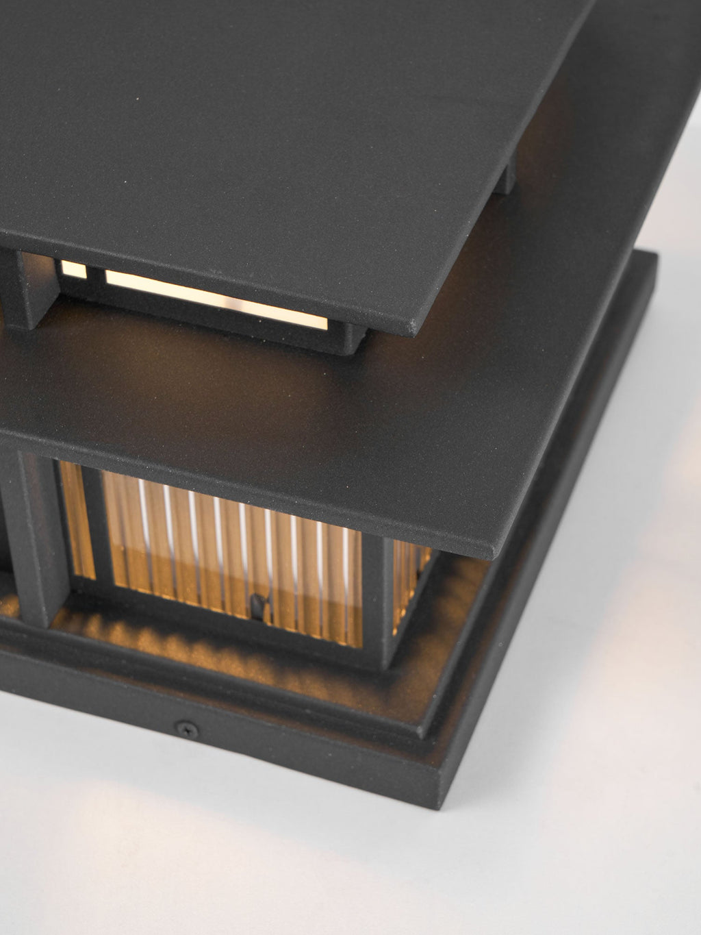 Close view of the layered aluminium roof and glowing top panel on this lit Clérachic pillar light.