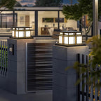 At a different angle, two lit Clérachic pillar lights sit above matching concrete gate posts by a metal gate.