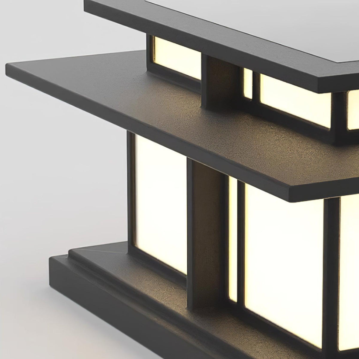 Angled view of this lit Clérachic pillar light, warm light spilling through its frosted glass panels against a textured grey backdrop.