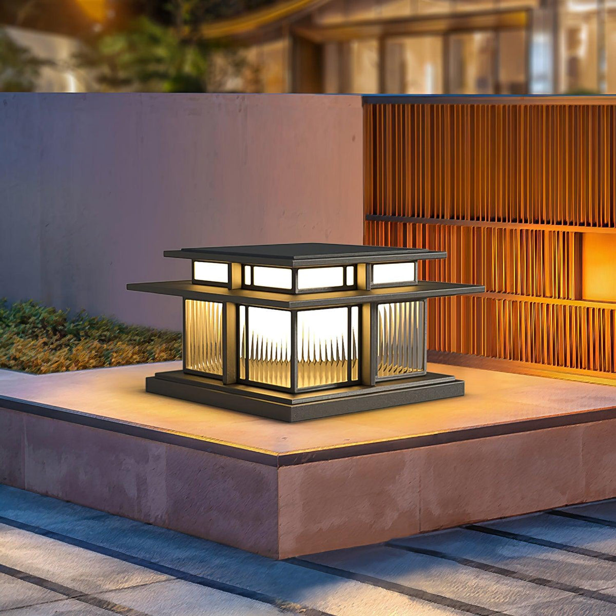 A lit Clérachic pillar light with fluted glass panels sits on a stone plinth beside a bamboo screen.