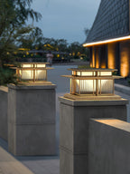 Two lit Clérachic pillar lights sit on paired concrete posts along a paved path leading toward a house at dusk.