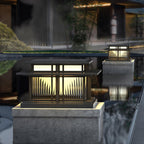 Fluted glass panels catch the light on this Clérachic pillar light, its reflection visible in the still water beside it.