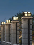 Under a deep blue evening sky, four lit Clérachic pillar lights line a row of concrete posts beside a metal fence.