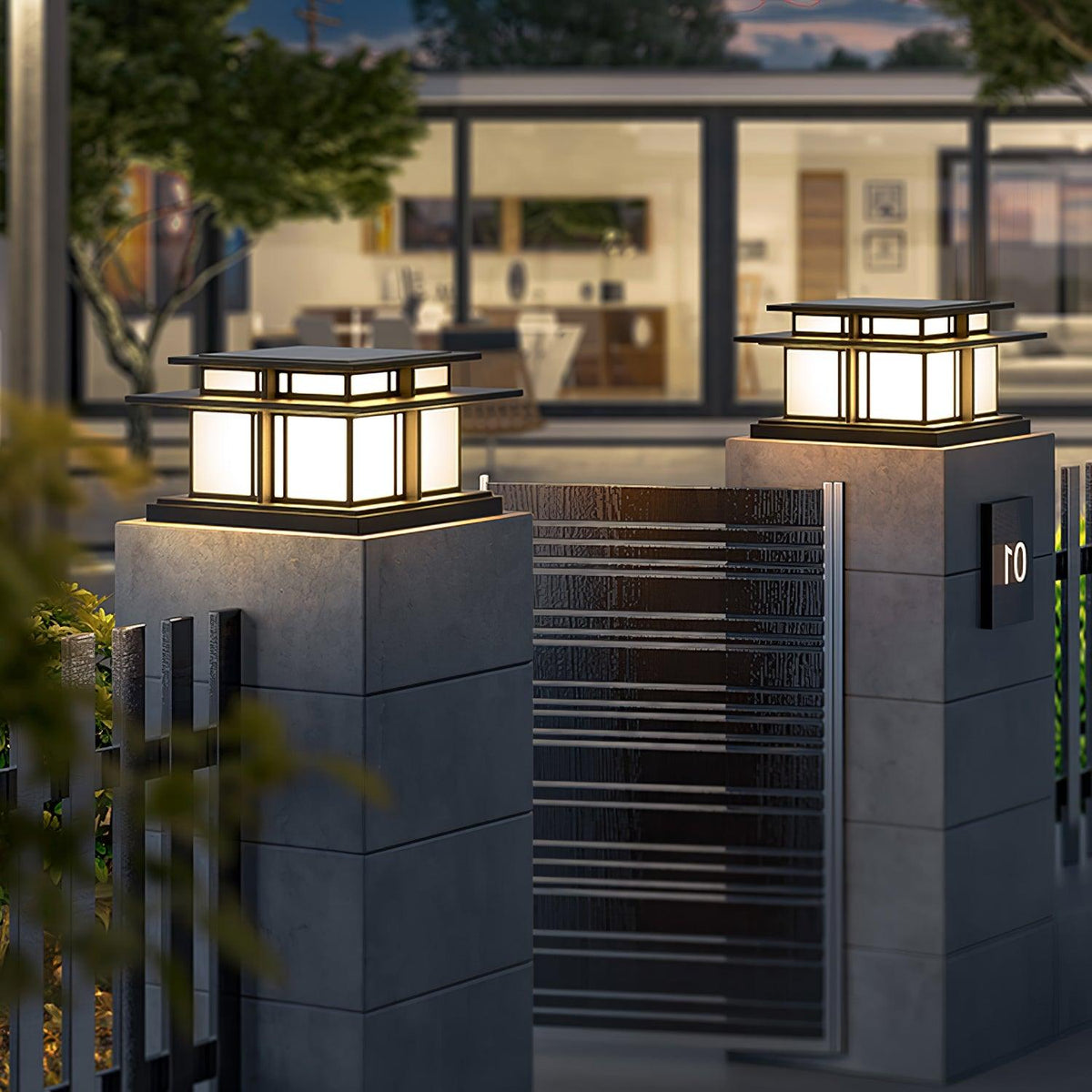 Two Clérachic pillar lights glow atop concrete gate posts in front of a glass-walled house at dusk.