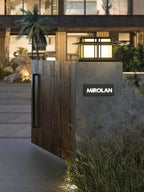 A lit Clérachic pillar light tops a plastered gatepost beside a timber gate panel, tropical planting at its base.
